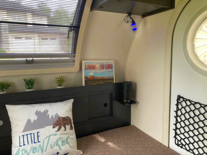 Inside a modern **rv rental**: a bed with a "Little Adventurer" pillow, magazine, plants, and Yeti holder.. Nucamp T@G 2022