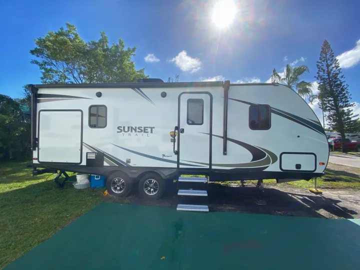 White Sunset Trail rv rental travel trailer parked in a sunny campground with green grass & trees.. Crossroads RV Sunset Trail Super Lite 2019