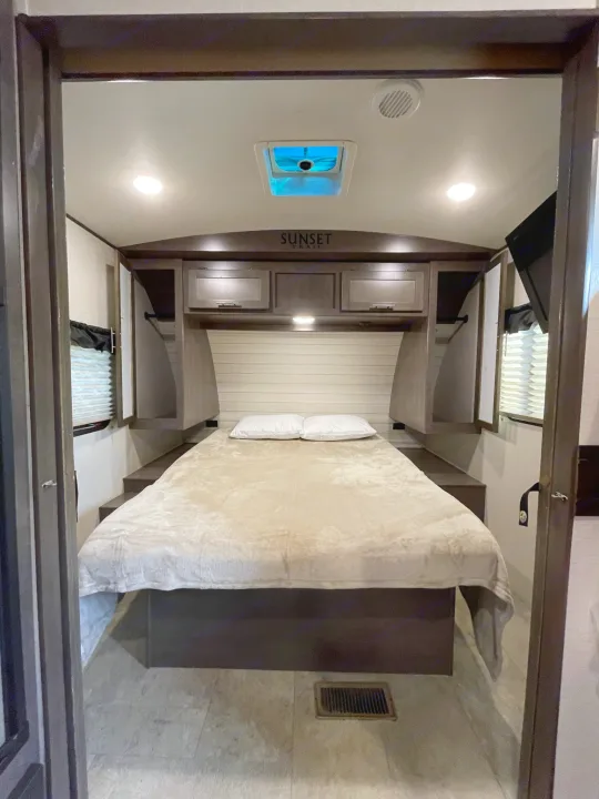 RV rental bedroom interior: bed, overhead cabinets, and windows with blinds. Ready for your road trip!. Crossroads RV Sunset Trail Super Lite 2019