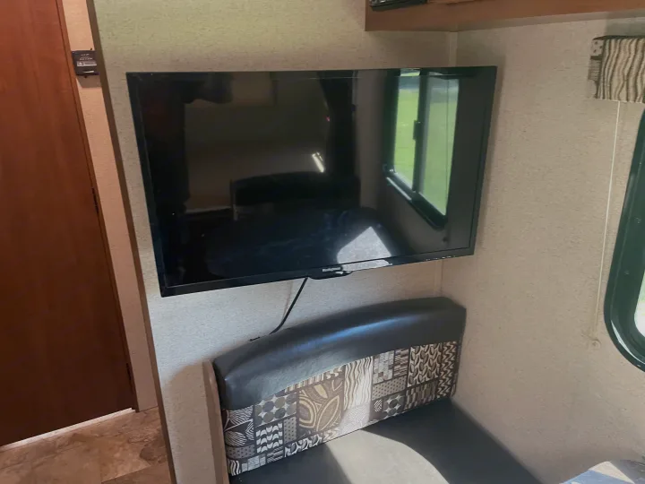 Enjoy your rv rental with this cozy interior, featuring a flat-screen TV, a patterned dinette bench, and a scenic window view.. Jayco Jay Flight SLX 2016