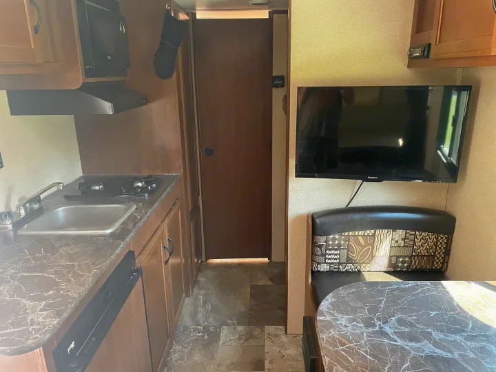 RV rental interior shows a kitchen with microwave, sink, and stovetop, plus a dining booth with TV.. Jayco Jay Flight SLX 2016