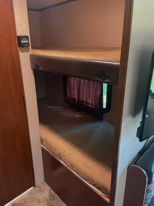 Inside an RV rental: a cozy sleeping area with two bunk beds, a window with curtains, and a control panel for comfort.. Jayco Jay Flight SLX 2016