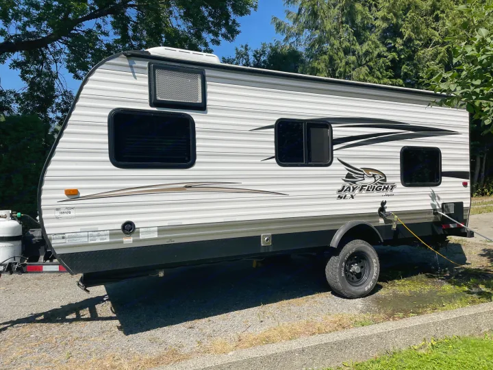 White Jayco Jay Flight travel trailer (RV rental) at a sunny campsite on gravel, with water pooling near the rear.. Jayco Jay Flight SLX 2016