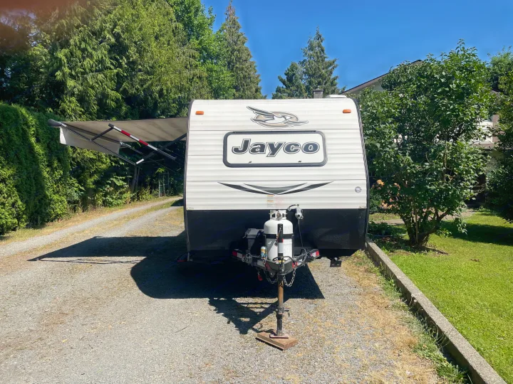 White Jayco travel trailer with awning deployed, parked on a gravel driveway. Ideal RV rental for your next outdoor adventure.. Jayco Jay Flight SLX 2016
