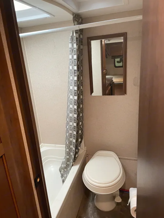 This RV rental bathroom features a compact shower with a curtain, a toilet, and a mirror reflecting the interior.. Jayco Jay Flight SLX 2016