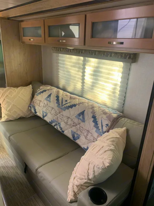 Cozy RV rental interior: sofa with decorative pillows, patterned blanket, overhead storage, and bright window.. R-Pod Hood River Edition 2020