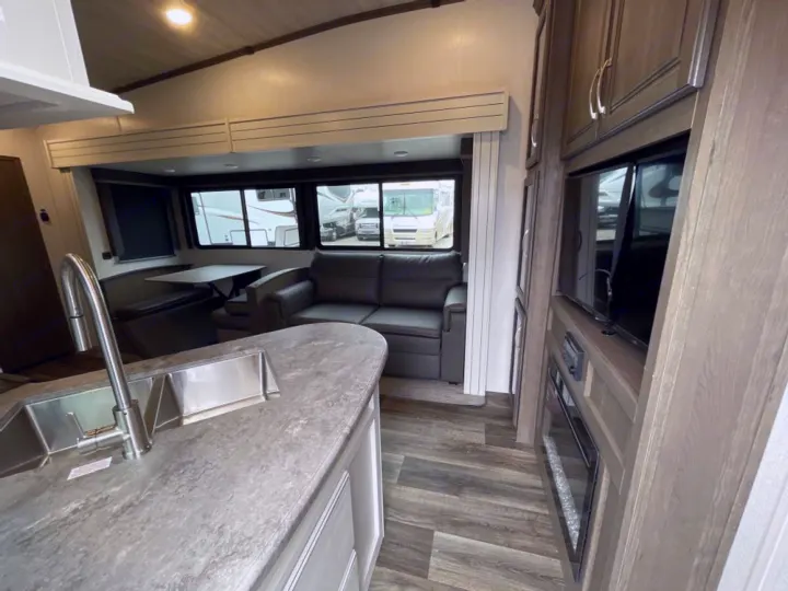 Explore a modern RV rental interior with a fully equipped kitchen island, dinette, sofa, and entertainment center.. Keystone RV Cougar 32BHS 2021