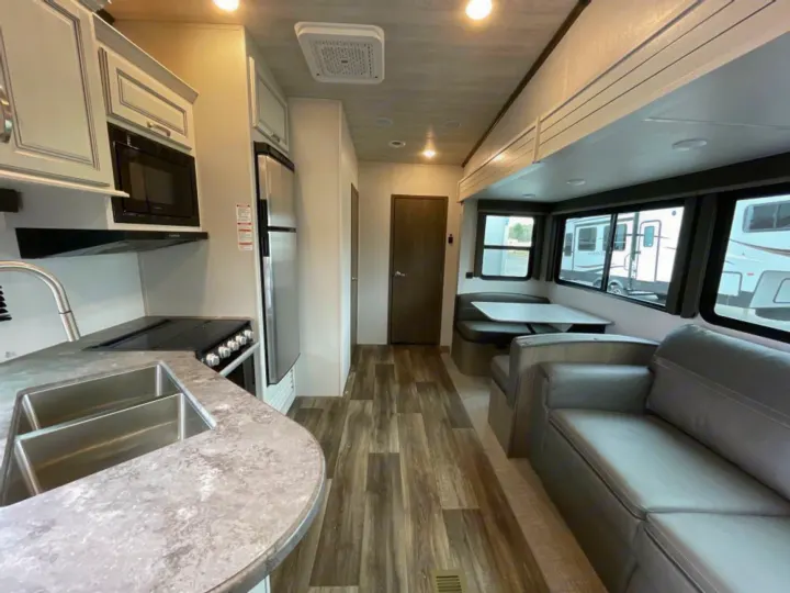Clean RV rental interior showcasing a kitchen with double sink, dining booth, and sofa. Ready for your road trip!. Keystone RV Cougar 32BHS 2021