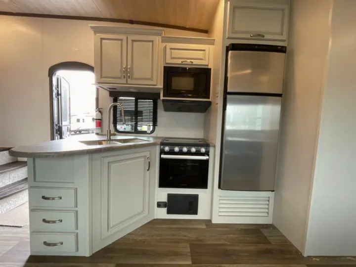 Spacious RV rental kitchen features light cabinets, stainless steel fridge, microwave, oven, and sink.. Keystone RV Cougar 32BHS 2021