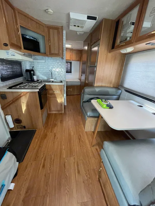 An RV rental interior showing the kitchen with a white subway tile backsplash, a dinette, and a bed in the rear.. Coachmen Catalina Sport 2002