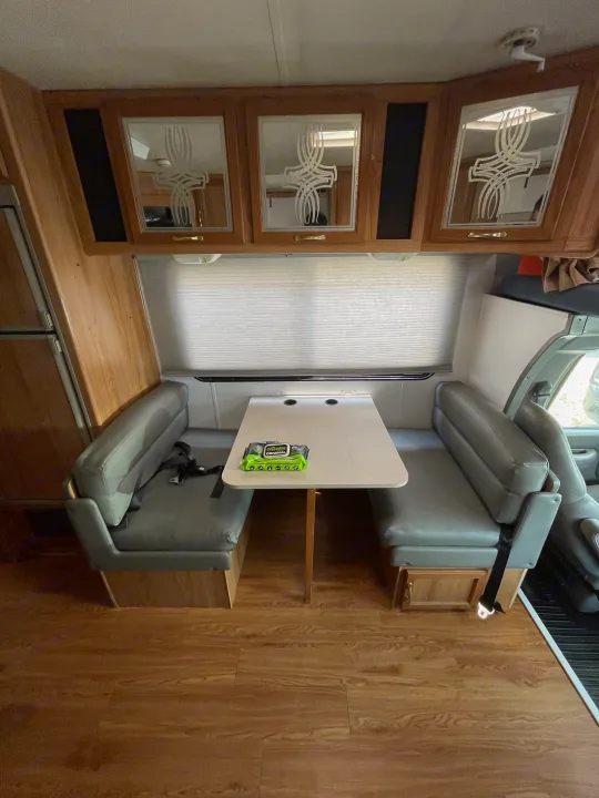 RV rental interior showing a cozy dinette with booth seating, table, overhead cabinets, and wood flooring.. Coachmen Catalina Sport 2002