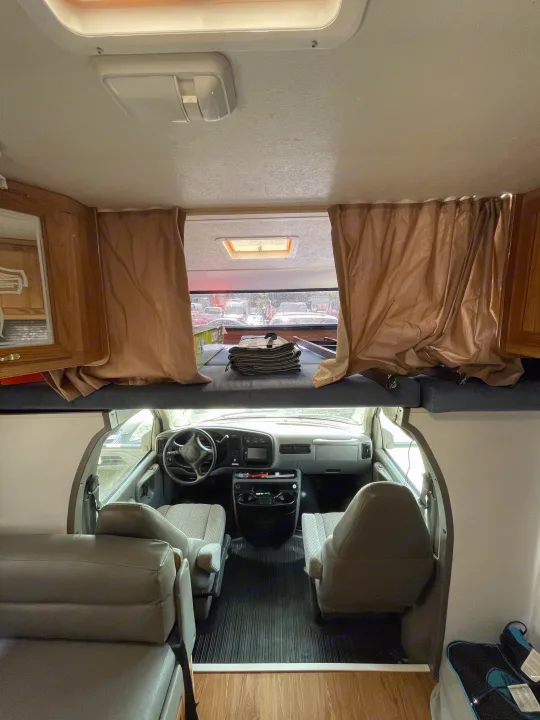 Inside an RV rental: view from living area to the front cab, showing the cab-over bunk, curtains, and driver's cabin.. Coachmen Catalina Sport 2002
