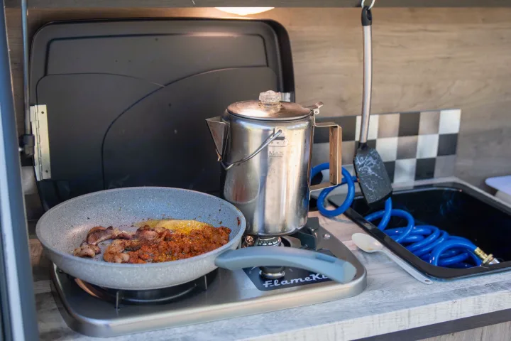 RV rental: Compact kitchen with stove, pan of food, coffee pot, and sink. Ready for camping meals!. Braxton Creek Free Solo 2022