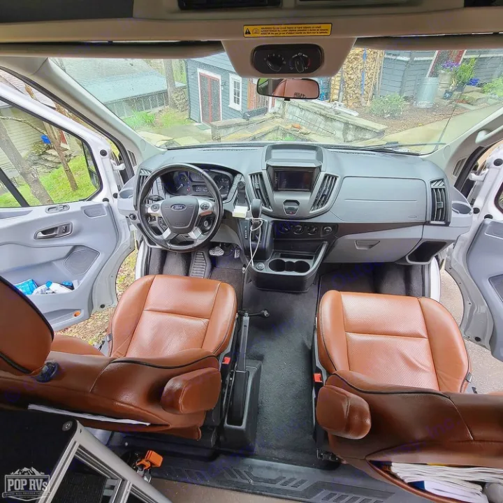Inside a modern RV rental van: spacious front cabin with brown leather captain's chairs and a clean dashboard.. Vandoit Vandoit Class B 2017