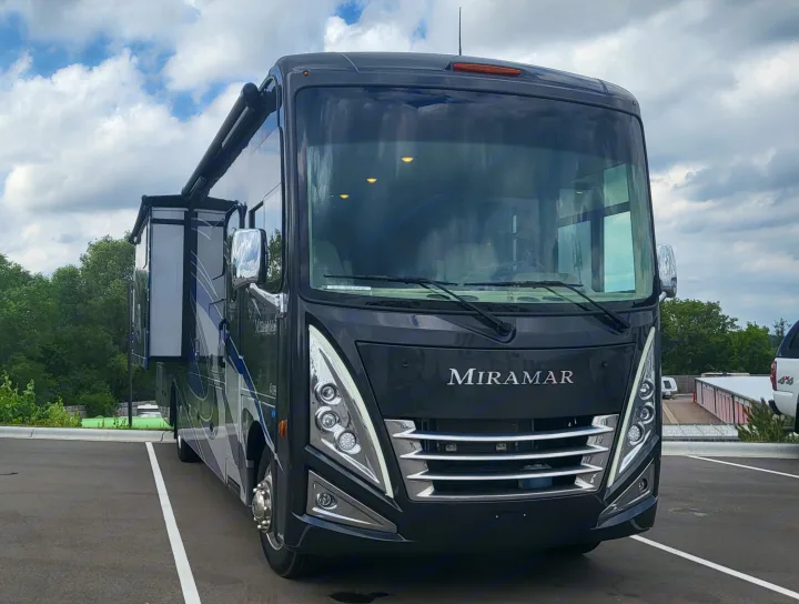 Front view of a large, dark gray Miramar motorhome parked on asphalt. Its awning is extended, ideal for an an RV rental adventure.. Thor Miramar 2022