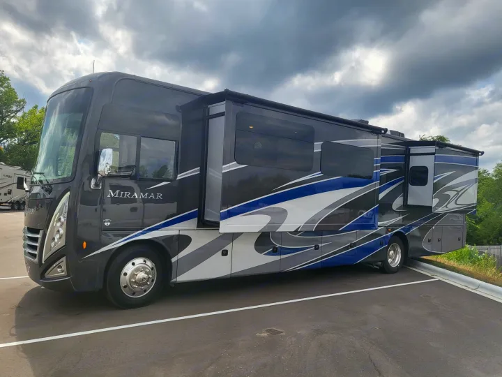 Modern dark grey RV rental, a Thor Miramar motorhome with blue/grey graphics, parked in a lot. Ideal for road trips under cloudy skies.. Thor Miramar 2022