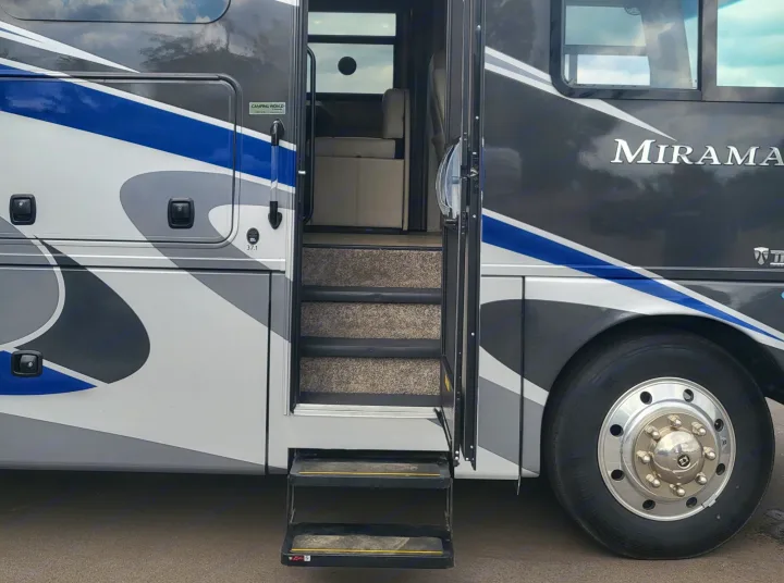 Side view of a grey and blue rv rental with its door open, revealing entrance steps and a glimpse of the interior.. Thor Miramar 2022