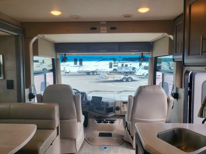 This RV rental's interior highlights the front dashboard, captain's chairs, and integrated living space with a dinette and sink.. Thor Miramar 2022