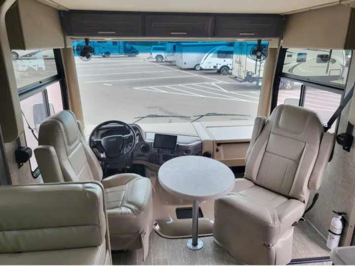 Step into this RV rental's comfortable cabin with swiveling captain chairs, small table, and view of other RVs.. Thor Miramar 2022
