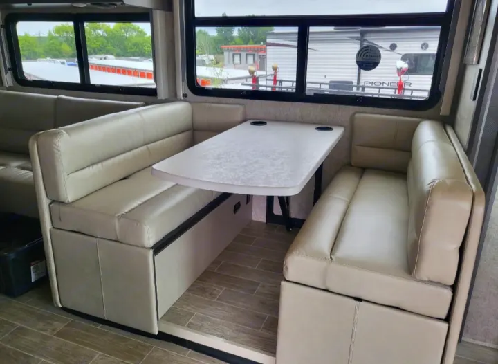 Spacious RV rental dinette featuring light-colored benches, a table with cup holders, and large windows.. Thor Miramar 2022