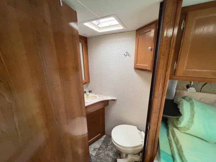 Explore a cozy RV rental bathroom featuring a toilet, sink, vanity, and overhead cabinets within a compact interior.. Coachmen Leprechaun 2019