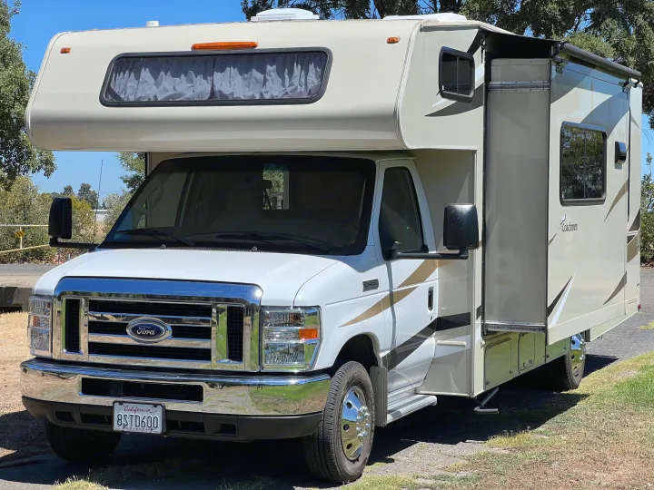 A cream and white Ford Class C motorhome, ideal for rv rental, parked outdoors. Features include a large slide-out and prominent front grille.. Coachmen Leprechaun 2019