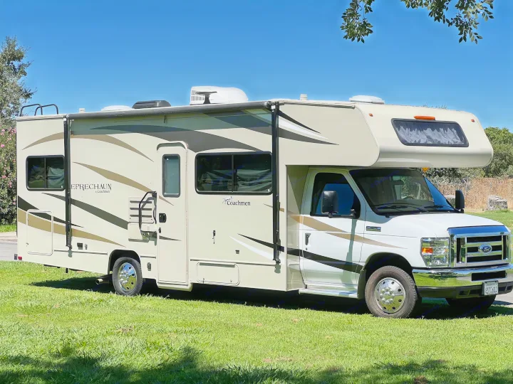 Sunny day showcases a tan Class C Coachmen Leprechaun rv rental on green grass.. Coachmen Leprechaun 2019