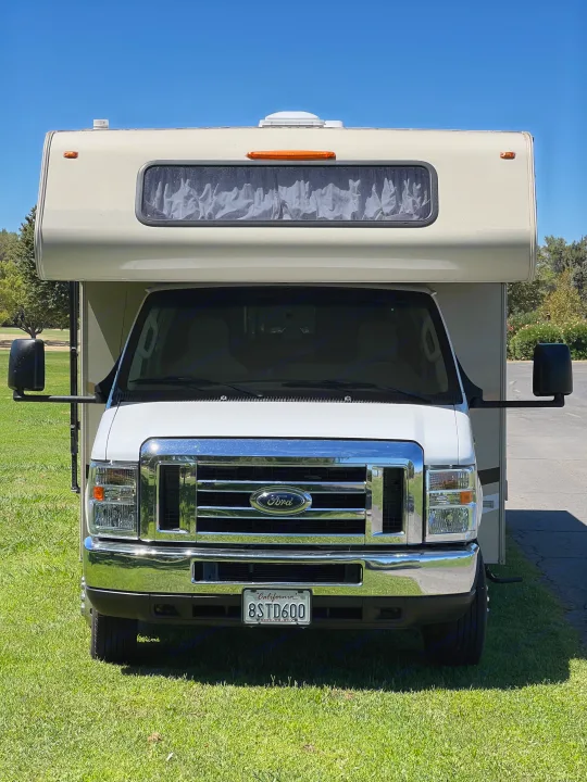 Bright front view of a white rv rental motorhome on green grass, ready for your next adventure under a clear sky.. Coachmen Leprechaun 2019