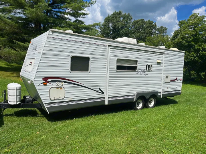 Jayco Eagle travel trailer, a spacious RV rental, parked on vibrant green grass under a sunny, partly cloudy sky.. Jayco Eagle 2003