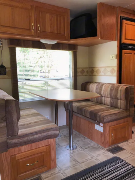 RV rental interior features a cozy dinette with patterned seats, a table, wooden cabinets, and a window.. Jayco Eagle 2003