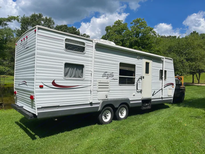 Experience nature with this RV rental: a white Jayco travel trailer parked on lush green grass by a calm pond.. Jayco Eagle 2003