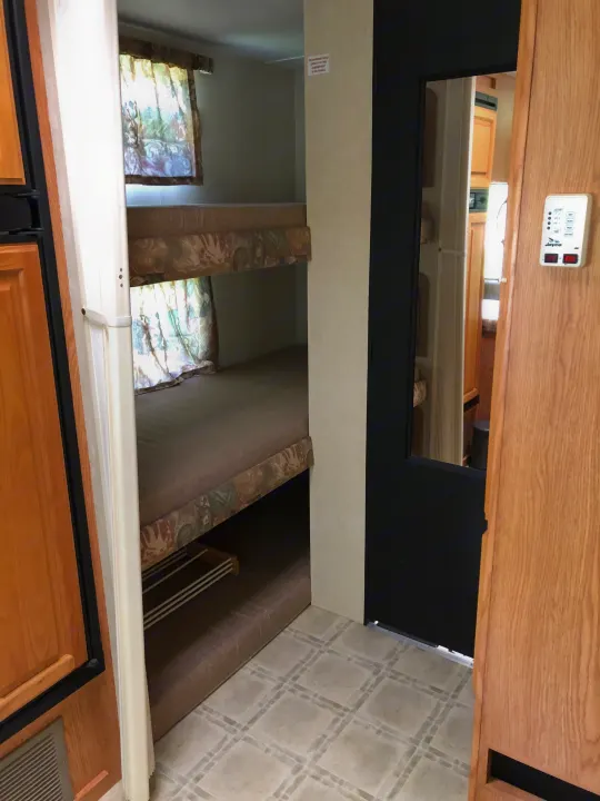 Cozy RV rental interior showcasing two bunk beds, a window with curtains, and tile flooring. Ideal for family trips.. Jayco Eagle 2003