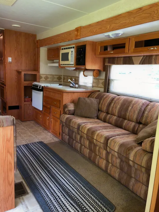 RV rental interior showcasing a kitchen with microwave/stove, patterned sofa, wood cabinets, and mixed flooring.. Jayco Eagle 2003
