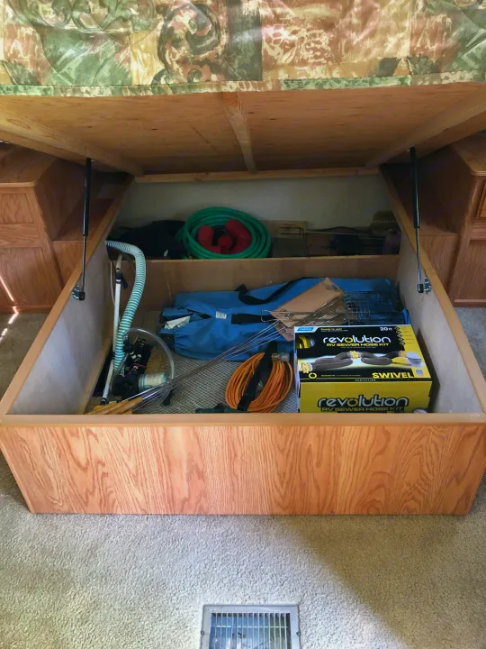 RV rental under-bed storage reveals essential camping gear like hoses and a sewer kit, perfect for travel organization.. Jayco Eagle 2003