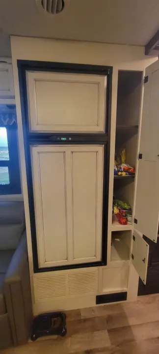 Inside an RV rental: Refrigerator, pantry with food, and dog bowl visible in the living area.. Jayco Greyhawk 2021