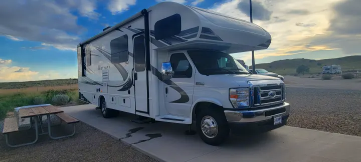 A white Jayco Greyhawk RV rental is parked at a scenic campground site with a picnic table under a partly cloudy sky.. Jayco Greyhawk 2021