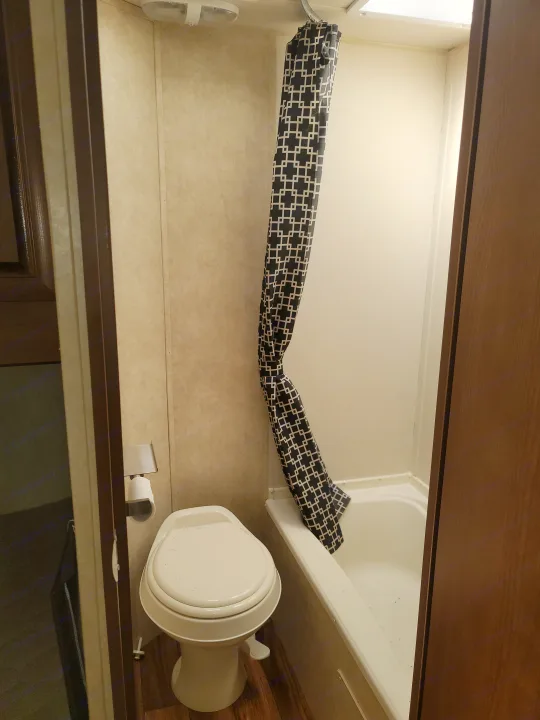 Compact RV rental bathroom: white toilet, shower with black/white geometric curtain, and accessible layout.. Forest River Salem 2016