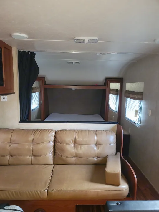 Bright RV rental interior featuring a large, tufted light brown leather sofa, windows, and wood cabinetry.. Forest River Salem 2016
