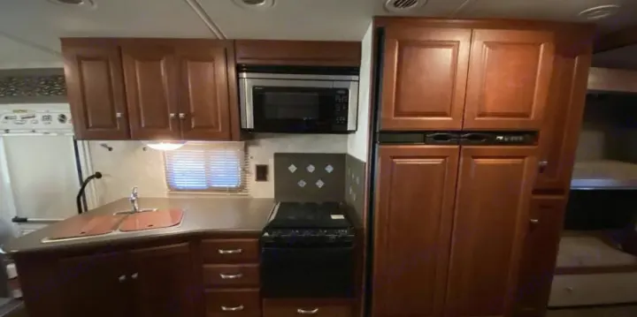 Spacious RV rental kitchen: wood cabinets, microwave, fridge, sink, stove, & adjacent bunk beds. Ready for adventure!. Itasca Sunstar 2013