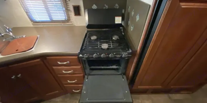Compact RV rental kitchen features a two-burner stove, open oven, and sink. Ideal for travel cooking.. Itasca Sunstar 2013