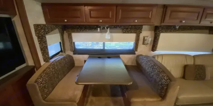 Comfortable RV rental interior featuring a dinette, overhead cabinets, a sofa, and window views. Perfect for your next trip.. Itasca Sunstar 2013