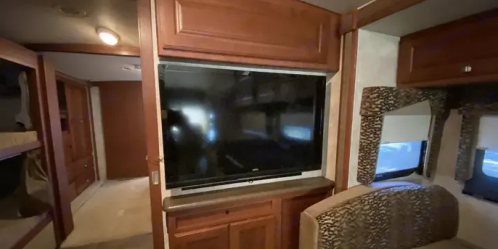 Spacious RV rental interior with TV, wooden cabinets, bunks, and patterned seating. Ideal for family adventures.. Itasca Sunstar 2013