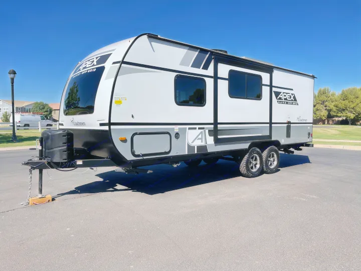 A sleek white and gray Coachmen Apex travel trailer, perfect for an RV rental, sits on asphalt.. Coachmen Apex 2022