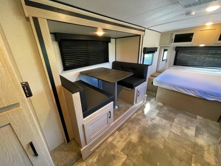 Clean RV rental interior: modern light wood dinette with black seats, grey table, and comfortable bed.. Coachmen Apex 2022