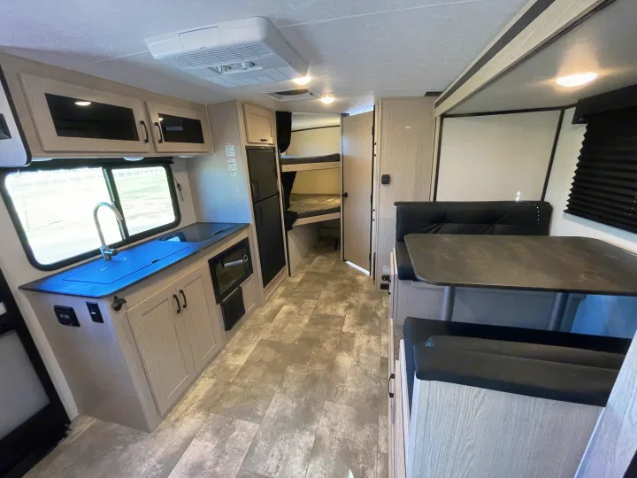 Clean RV rental interior: galley kitchen with sink, microwave, fridge, dinette, bunk beds, and overhead AC.. Coachmen Apex 2022