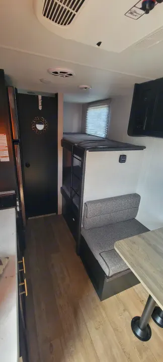 RV rental interior: bunk beds on the right, a grey cushioned dinette in front, and a partial view of the kitchen counter. Features wood-look flooring.. Forest River Cherokee Wolf Pup 2021