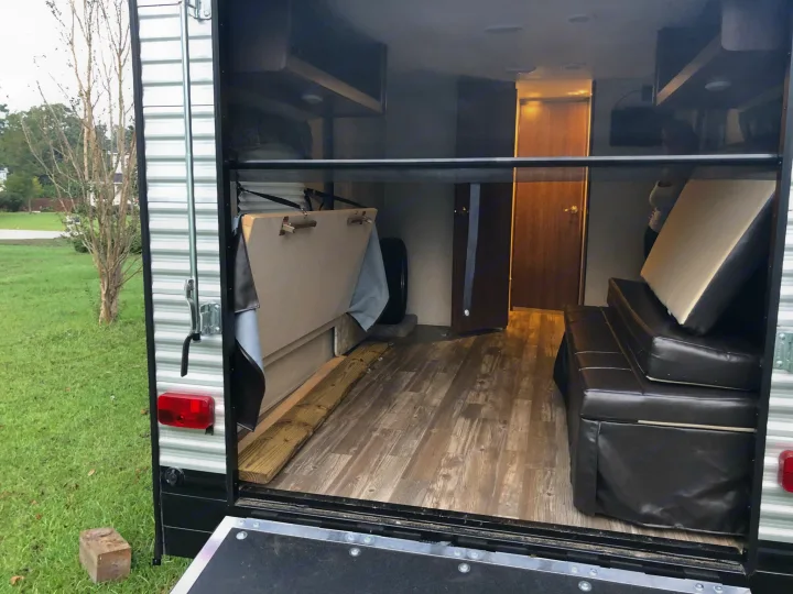 RV rental: An open toy hauler's interior reveals modular seating, wood-look flooring, and a folded bunk, viewed from the rear ramp.. Heartland RVs Pioneer Toy Hauler 2017