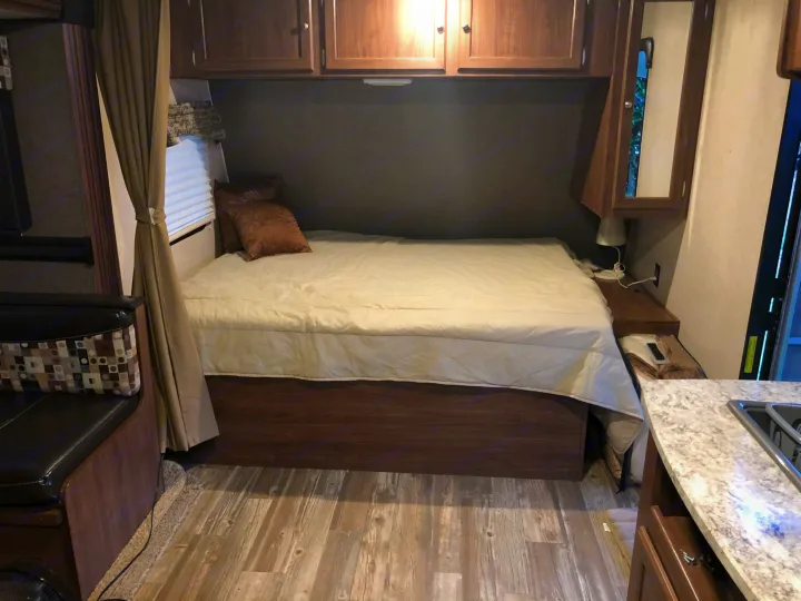 Compact RV rental interior featuring a cozy bedroom area with a bed, cabinets, and seating, plus a glimpse of the kitchen.. Heartland RVs Pioneer Toy Hauler 2017