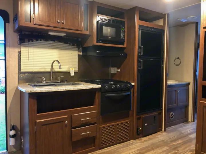 Compact RV rental kitchen features wood-look cabinets, sink, stove, oven, microwave, and fridge. Functional layout.. Heartland RVs Pioneer Toy Hauler 2017