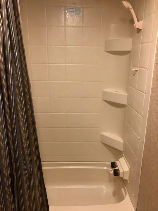 Clean white shower and tub combo in an RV rental, complete with a striped curtain, handheld shower, and shelves.. Heartland RVs Pioneer Toy Hauler 2017